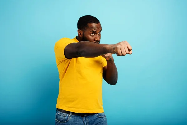 Black man punches and fight against something. cyan background — Stock Photo, Image