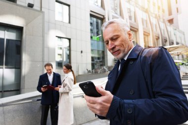 İş adamı elinde akıllı telefonla ofisin dışında.