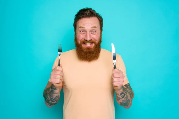 Homme heureux avec des tatouages est prêt à manger avec des couverts à la main — Photo