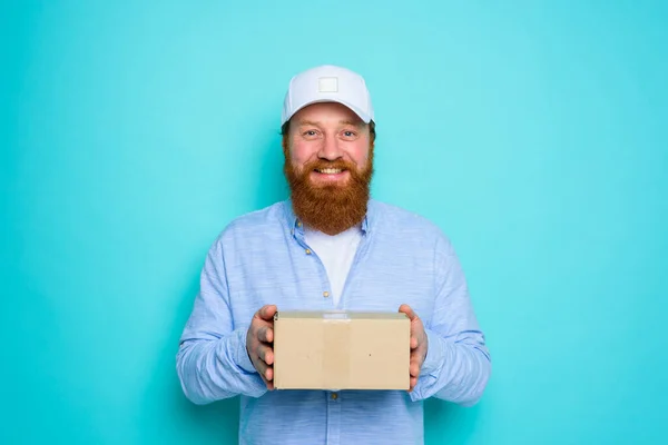 Courier com chapéu está feliz em entregar uma caixa de papelão — Fotografia de Stock