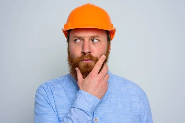 Isolated doubter architect with beard and orange helmet — Stock Photo, Image