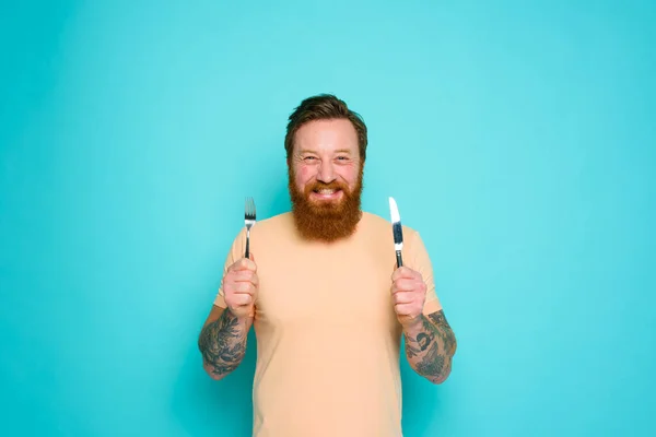 Szczęśliwy człowiek z tatuażami jest gotowy do jedzenia ze sztućcami w ręku — Zdjęcie stockowe