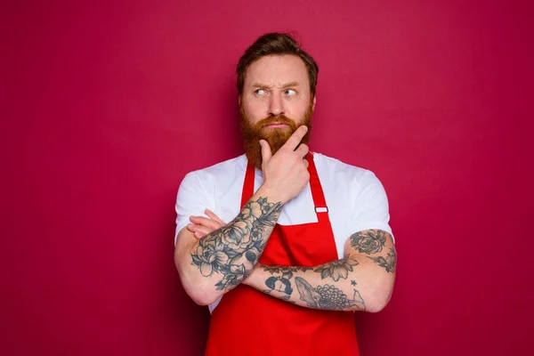 Doubter isolated chef with beard and red apron — Photo
