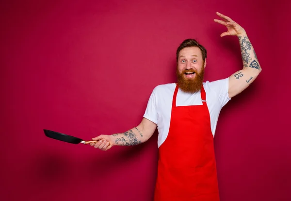 Felice chef con barba e grembiule rosso cuochi con padella — Foto Stock