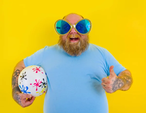 Grubas z brodą i okularami przeciwsłonecznymi zabawia się piłką — Zdjęcie stockowe