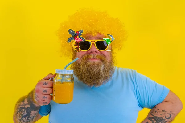 Fat happy man with wig in head and sunglasses drinks a fruit juice — Stock Photo, Image