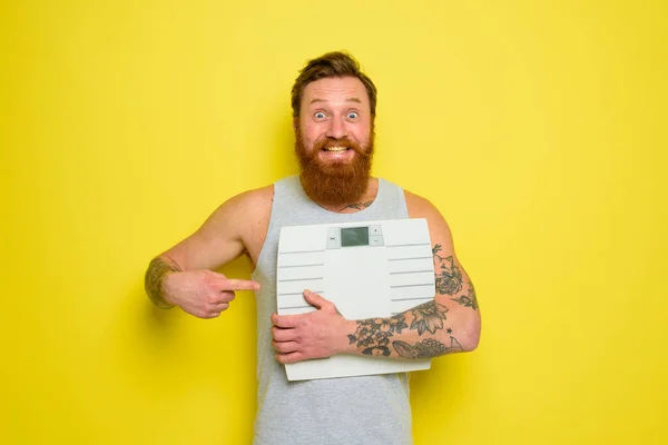 Amazed man with beard and tattoos holds an electronic balance — Stock Photo, Image