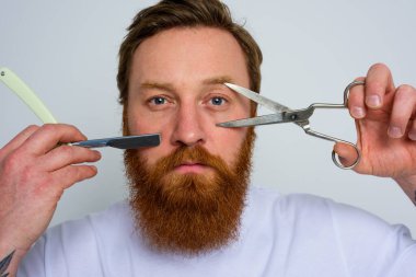 Makas ve bıçaklı endişeli adam sakalı kesmeye hazır.