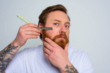 Serious man with blade is focused on cutting his beard clipart