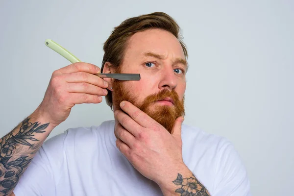 Hombre serio con la hoja se centra en cortar su barba — Foto de Stock