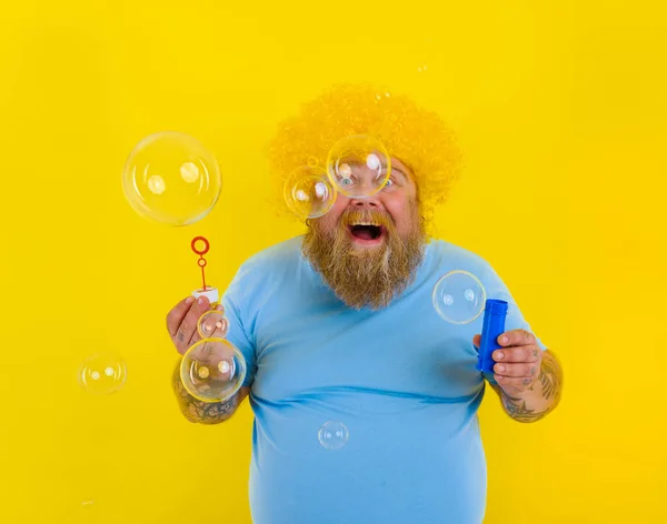 Εντυπωσιασμένος άντρας με κίτρινη περούκα στο κεφάλι να παίζει με σαπουνόφουσκες — Φωτογραφία Αρχείου