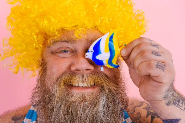 Grasso uomo felice con barba e occhiali da sole divertirsi con un giocattolo di pesce — Foto Stock