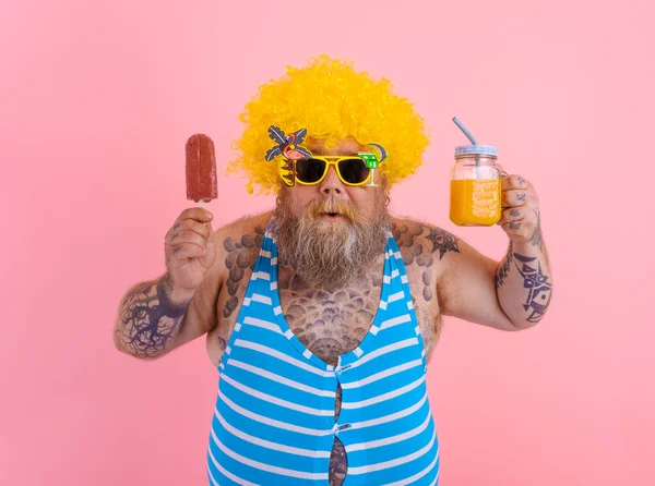 Grasso sorpreso uomo con barba e parrucca mangia un ghiacciolo e beve un succo di frutta — Foto Stock