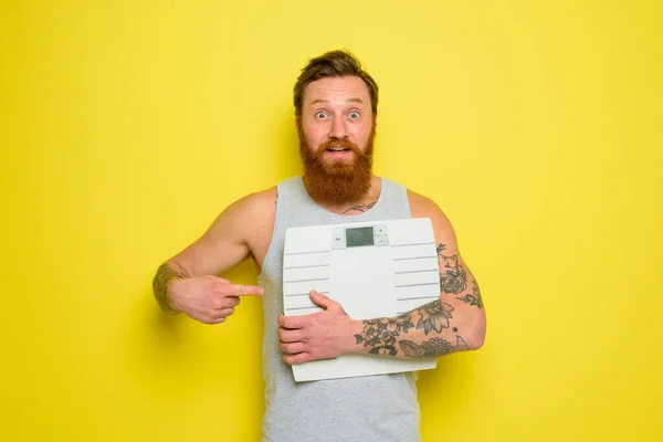 Amazed man with beard and tattoos holds an electronic balance — Stock Photo, Image