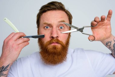 Makas ve bıçaklı endişeli adam sakalı kesmeye hazır.