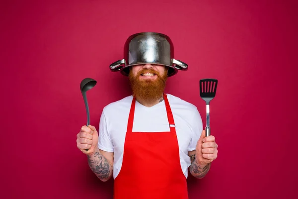 수염을 기르고 붉은 앞치마를 입은 행복 한 요리사가 요리할 수있다 — 스톡 사진