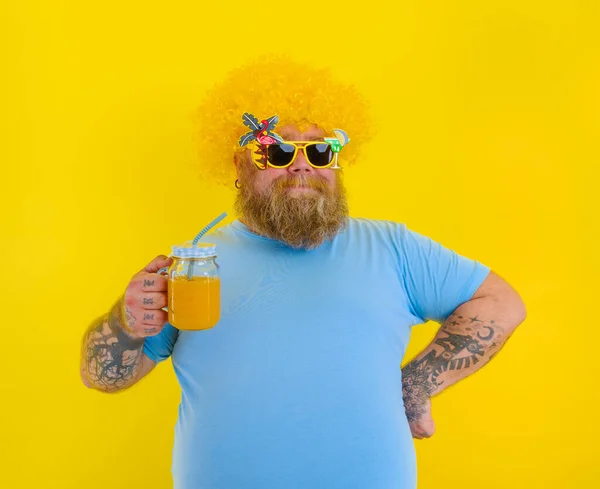 Tłuszcz szczęśliwy człowiek z peruką w głowie i okularach przeciwsłonecznych pije sok owocowy — Zdjęcie stockowe