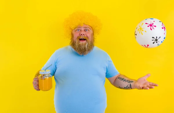 Tłuszcz szczęśliwy człowiek z peruką w głowie i okularach przeciwsłonecznych pije sok owocowy — Zdjęcie stockowe