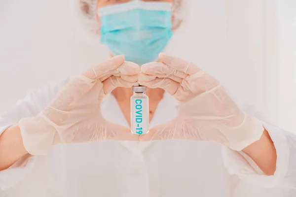 Maskeli bir doktor elleriyle ve kovid 19 aşısıyla kalp üretiyor. — Stok fotoğraf