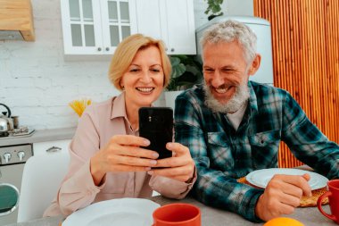 Çift kahvaltısını evde yapar ve akıllı telefondan bir şeyler okur.