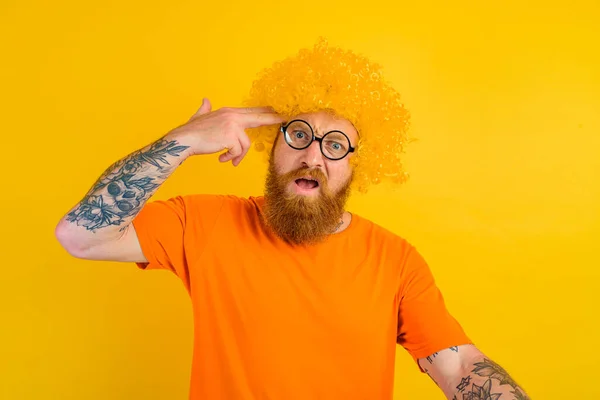 Mężczyzna w brodzie, żółtej peruce i okularach robi gestem pistoletu ręką — Zdjęcie stockowe