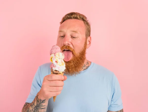 Uomo affamato con la barba e tatuaggi mangia un grande gelato — Foto Stock