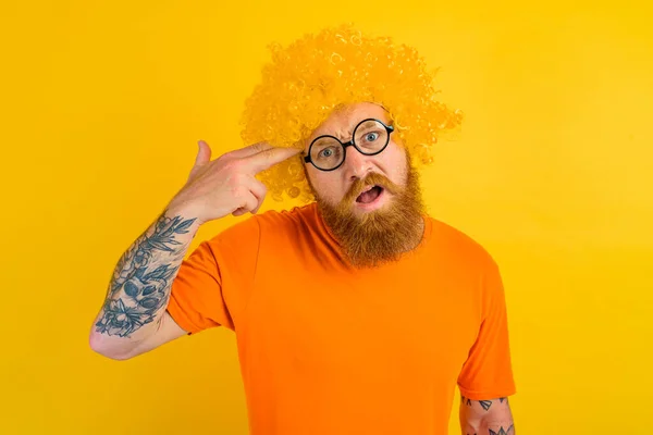 Uomo con barba, parrucca gialla e occhiali fa un gesto di pistola con la mano — Foto Stock