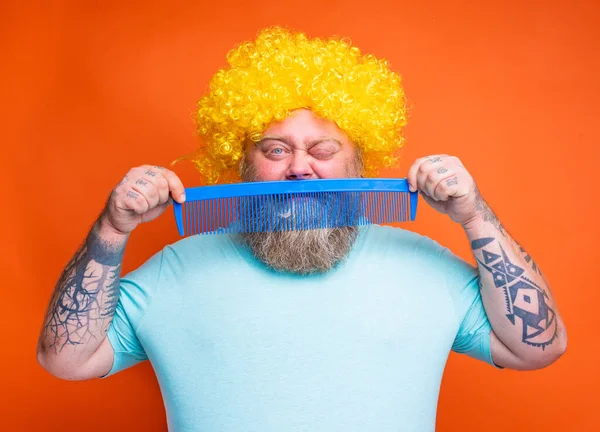Fat doubter man with beard, tattoos and sunglasses combs himself with a giant comb — 图库照片