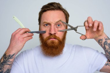 Makas ve bıçaklı endişeli adam sakalı kesmeye hazır.