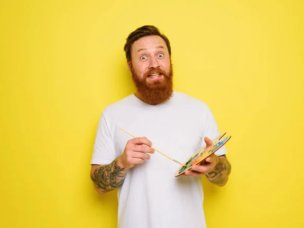 Doubter homem com barba e tatuagem está pronto para desenhar com escovas — Fotografia de Stock