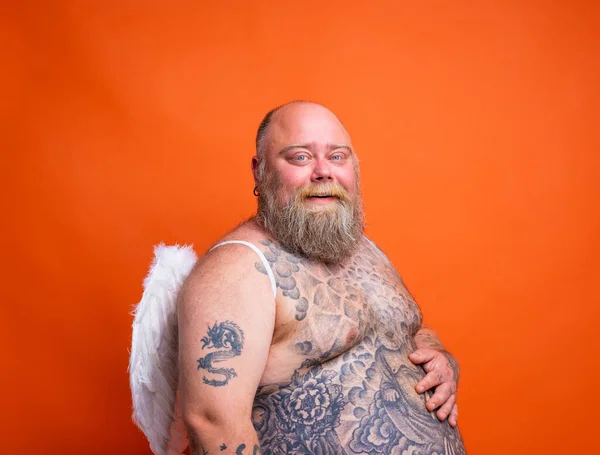 Gordo hombre feliz con barba, tatuajes y alas actúa como un ángel — Foto de Stock