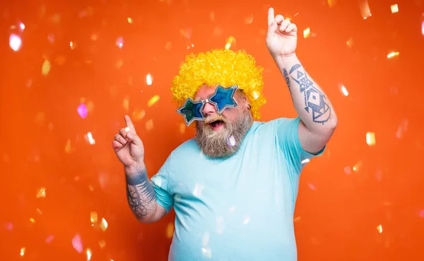 Fat man with beard, tattoos and sunglasses dances music on a disco