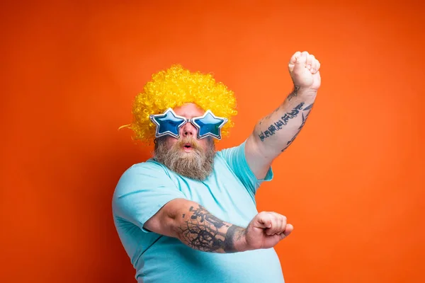 Fat man with beard, tattoos and sunglasses dances music on a disco