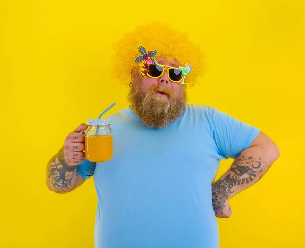 Fat happy man with wig in head and sunglasses drinks a fruit juice — Stock Photo, Image