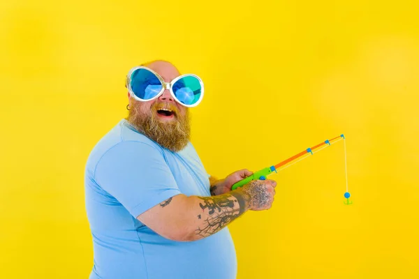 Grubas z brodą i okularami przeciwsłonecznymi bawi się wędką — Zdjęcie stockowe
