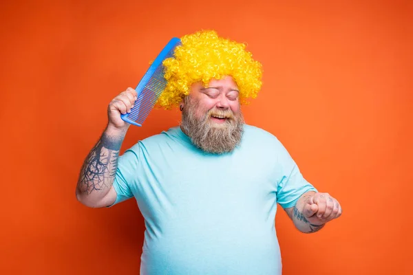 Grasso uomo felice con la barba, tatuaggi e occhiali da sole si pettina con un pettine gigante — Foto Stock