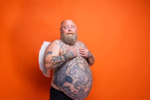 Hombre gordo asombrado con barba, tatuajes y alas actúa como un ángel — Foto de Stock