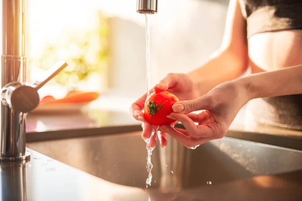 Kadın mutfaktaki domatesleri temizliyor. Güneşle aydınlatılıyor. — Stok fotoğraf
