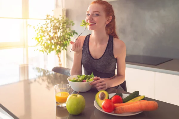 Αθλητική νεαρή κοκκινομάλλα γυναίκα στην κουζίνα σπίτι τρώει μια υγιεινή σαλάτα — Φωτογραφία Αρχείου