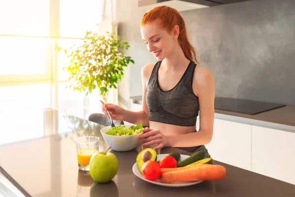 Atletica giovane donna dai capelli rossi in cucina mangiando un'insalata sana — Foto Stock