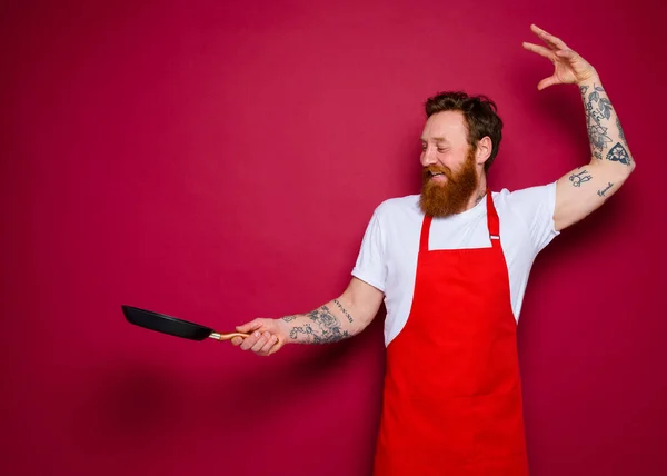 Felice chef con barba e grembiule rosso cuochi con padella — Foto Stock