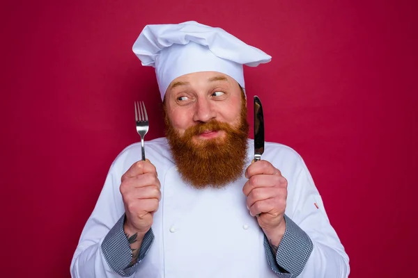 Szczęśliwy szef kuchni z brodą i czerwony fartuch trzyma sztućce w dłoni — Zdjęcie stockowe