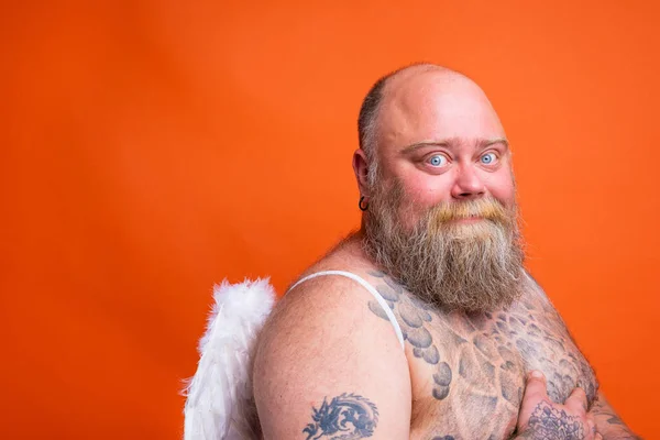 Fat happy man with beard ,tattoos and wings acts like an angel — Stock Photo, Image