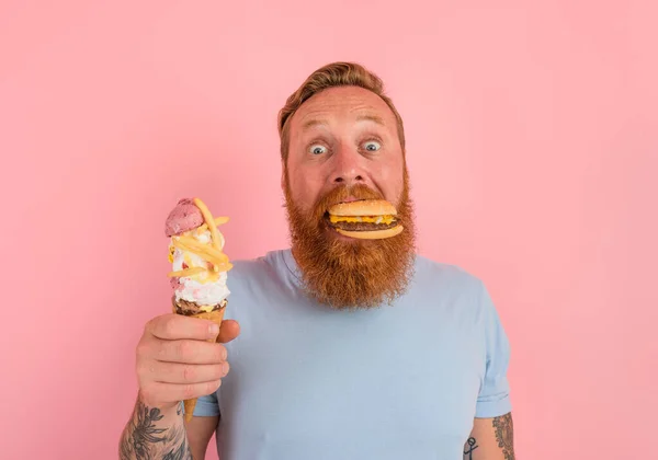 Hungriger Mann mit Bart und Tätowierungen ist unentschlossen, ob er ein Eis oder ein Sandwich mit Hamburger essen soll — Stockfoto