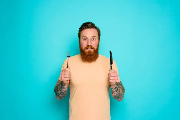 Happy man with tattoos is ready to eat with cutlery in hand — Stock Photo, Image