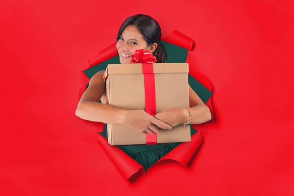 Woman inside a hole on a red paper backdrop holds tight in her arms a gift package — Stock Photo, Image