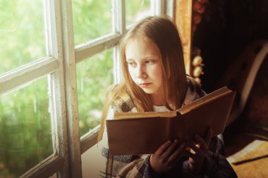 Köy kızı pencerenin kenarında bir kitapla.