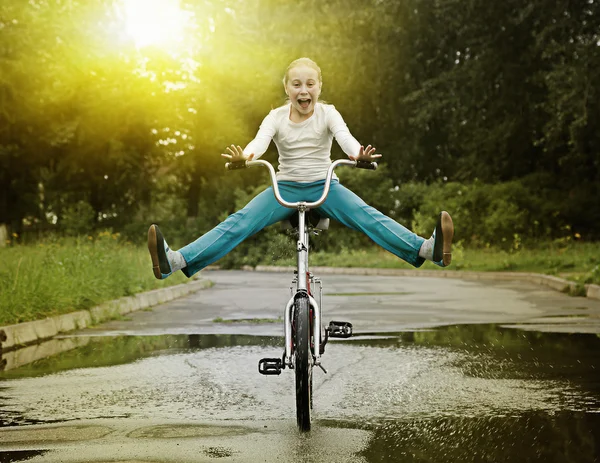 Dítě na kole projíždět kaluže. — Stock fotografie