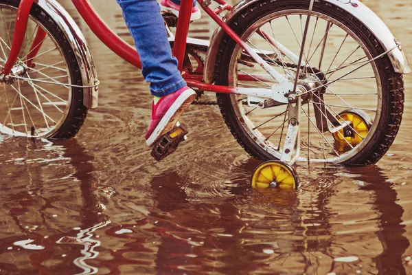 Criança em passeios de bicicleta através de uma poça no dia de outono . — Fotografia de Stock