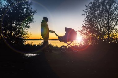 Gün batımında bir kız bir sonbahar günü bebek arabasında bir bebekle yürür..